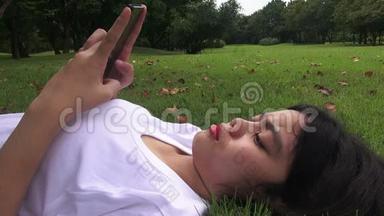高清格式：年轻女子躺在草地上发短信，在公园发短信。